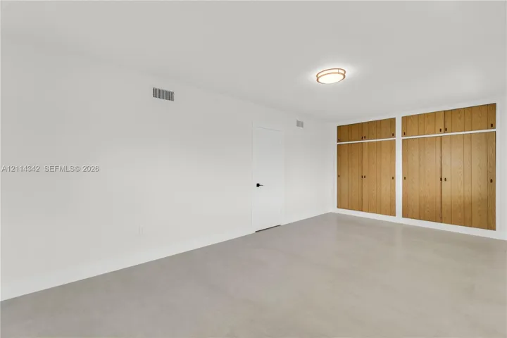 Neutral-toned flooring, expansive wall-to-wall built-in wood cabinetry, and a flush-mount circular ceiling fixture