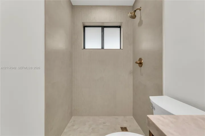 Walk-in shower featuring large-format stone-finish tile surround, metallic finish showerhead and hardware, built-in window, and hexagonal floor tile