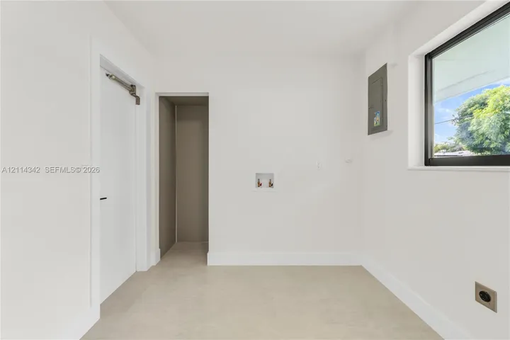 Utility room featuring neutral tile flooring, a window with a black frame, recessed doorway, and dedicated water hookups