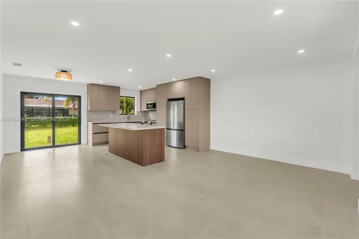 Open-concept kitchen featuring flat-panel cabinetry, a central island with stone-finish countertops, stainless steel appliances, recessed lighting, and sliding glass doors