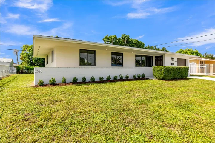 Mid-century modern exterior featuring a low-slope roof, crisp white stucco finish, recessed soffit lighting, and manicured foundation plantings