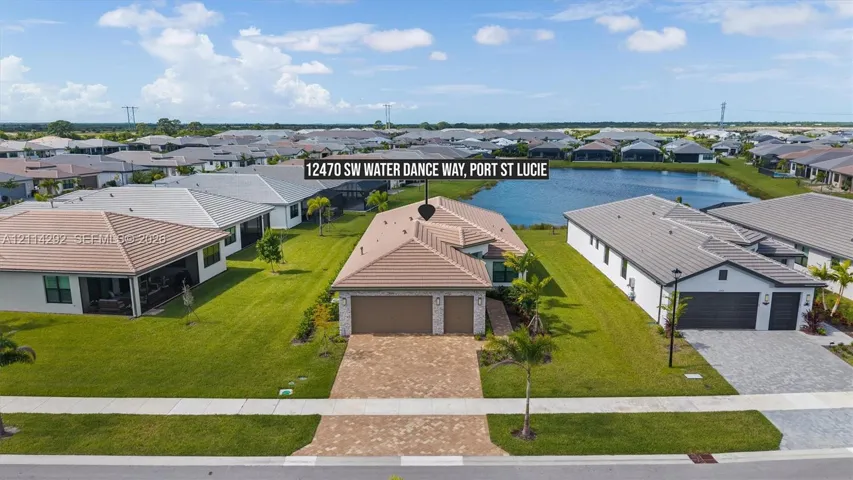 Aerial perspective of a single-story residence featuring a tiled roof, multi-car garage, paver driveway, and a backyard water feature