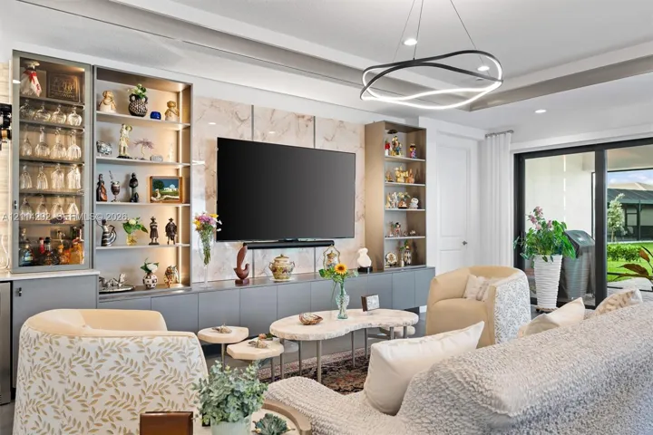 Custom built-in cabinetry featuring illuminated glass-front display shelving, stone-patterned accent wall, modern multi-ring chandelier, tray ceiling, and sliding glass patio doors