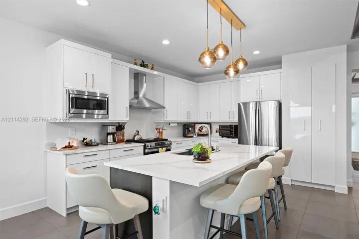 Kitchen featuring white high-gloss cabinetry, a central island with a stone countertop, stainless steel appliances, recessed ceiling lighting, and multi-globe pendant fixtures