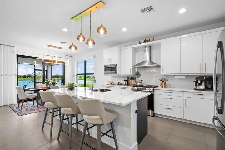Kitchen featuring high-gloss white cabinetry, a large central island with white quartz countertops, stainless steel appliances, and multi-pendant lighting
