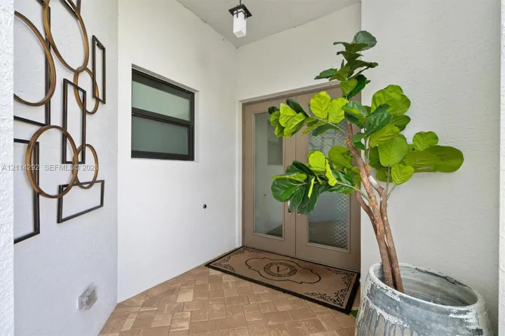 Covered entryway featuring herringbone-patterned stone flooring, a double-door entry with frosted glass inserts, and a contemporary ceiling-mounted lantern fixture