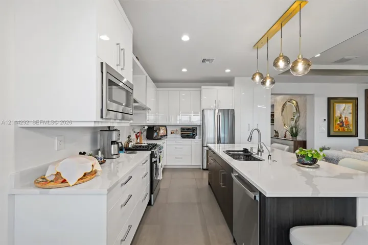 Kitchen featuring high-gloss white cabinetry, expansive stone countertops, stainless steel appliances, a central island, and modern pendant lighting