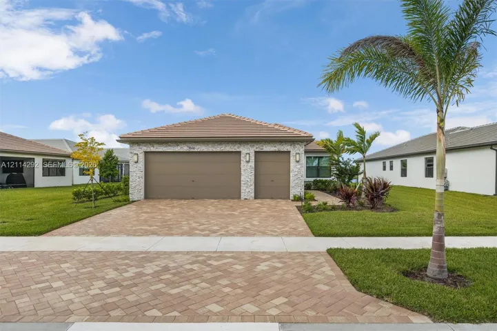 Exterior featuring stone veneer facade, tile roof, three-car garage, and paver driveway