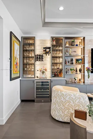 Built-in wet bar featuring custom cabinetry, integrated wine refrigerator, recessed display shelving with internal lighting, and a textured stone backsplash