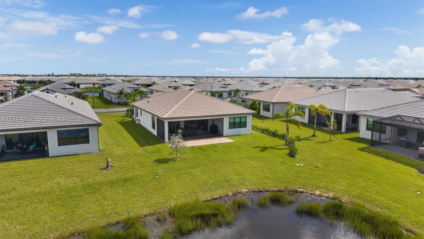 Single-story residence featuring a tile roof, covered rear patio, and expansive lawn area overlooking a retention pond