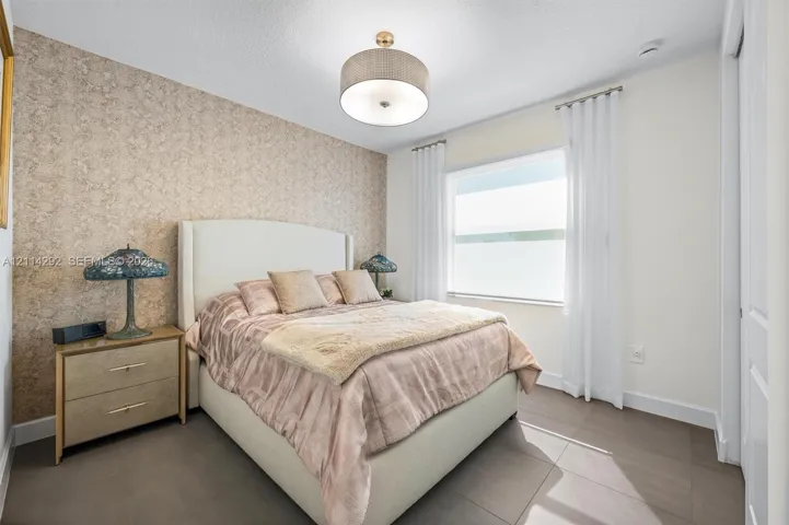 Textured accent wall, large window with neutral-toned treatments, drum-style ceiling light fixture, and ceramic tile flooring