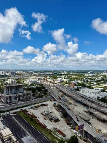 High-elevation aerial perspective featuring an expansive cityscape, multi-level roadway infrastructure, and integrated surface parking