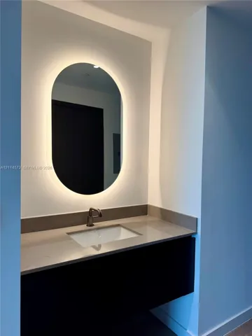 Floating vanity with stone countertop, undermount sink, metallic faucet, and oval back-lit mirror
