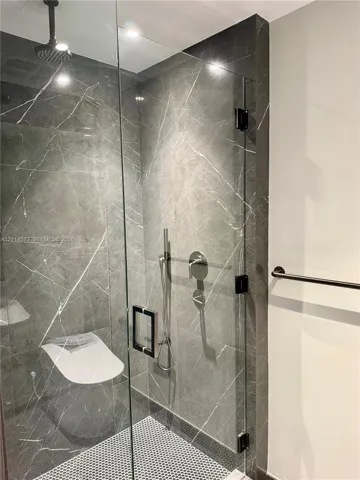 Walk-in shower featuring large-format stone-look wall tiles, mosaic floor tiling, frameless glass enclosure, ceiling-mounted rainfall showerhead, and adjustable hand-held sprayer