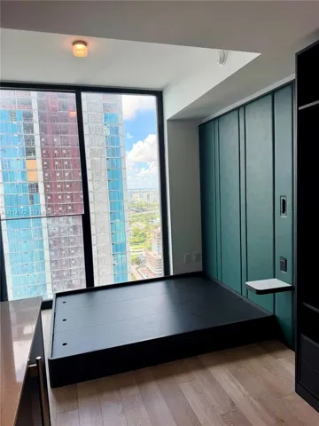 Floor-to-ceiling windows, custom green paneled wall with integrated shelving, built-in elevated platform, and wood-finish flooring