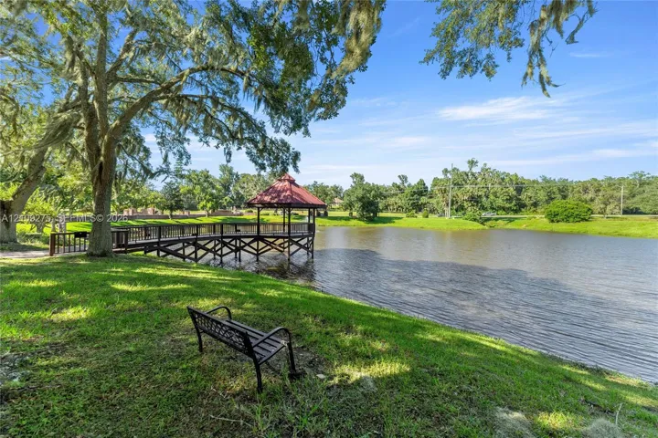 Waterfront grounds featuring a wooden pier with a covered gazebo, expansive lawn, and mature oak trees