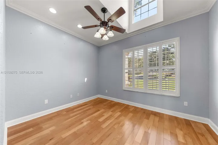 Room featuring vaulted ceilings, wood-finish flooring, multi-pane transom window, plantation shutters, and a ceiling fan with integrated light fixtures