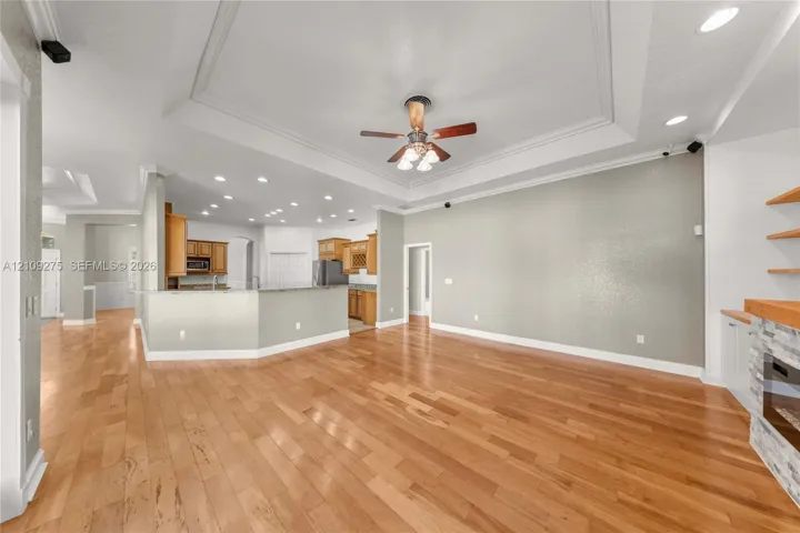 Open floor plan featuring a tray ceiling, recessed lighting, wood-finish flooring, a kitchen peninsula, and a stone-accented fireplace