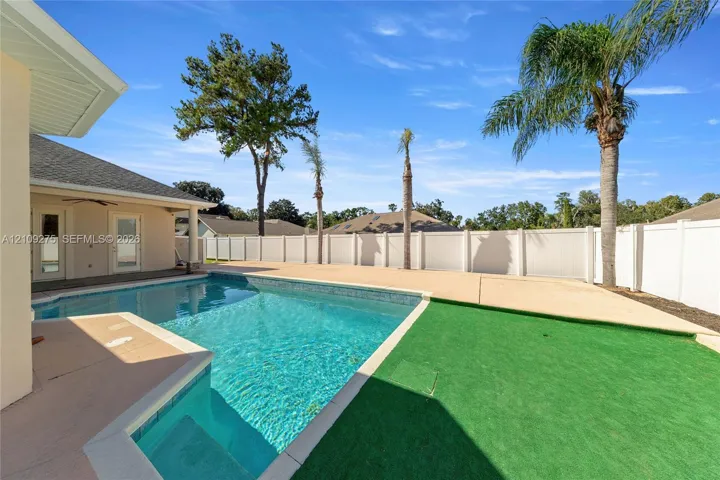 Swimming pool with built-in stairs, expansive concrete decking, synthetic turf area, and privacy fencing