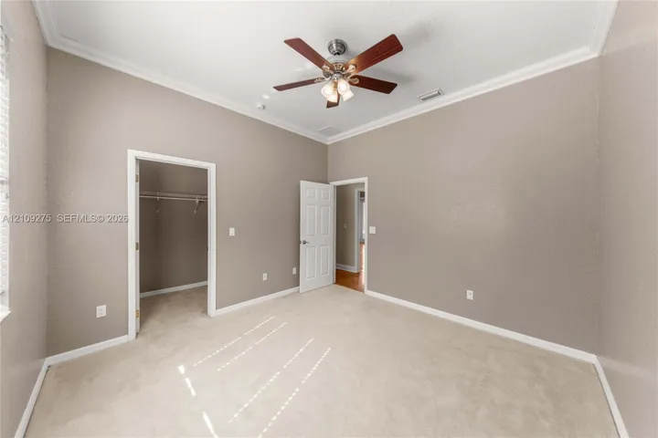High ceilings with crown molding, neutral carpeting, ceiling fan with integrated light fixture, and interior walk-in closet with built-in shelving