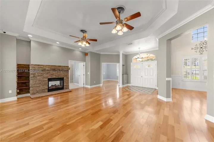 Spacious interior featuring wood-finish flooring, a stone-faced fireplace with built-in shelving, tray ceilings, and dual ceiling fans