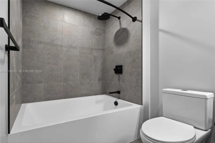 Bathroom featuring a white deep-basin tub, matte black shower head and faucet hardware, and full-height grey tile wall surround