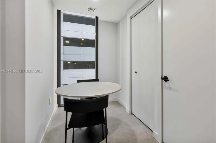 Neutral-toned interior space featuring large floor-to-ceiling windows, tile flooring, and white double-door closet storage with matte black hardware