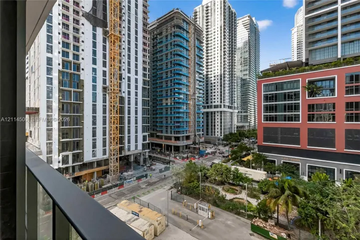 Balcony featuring a matte black metal railing overlooking an urban streetscape with high-rise structures and landscaped grounds