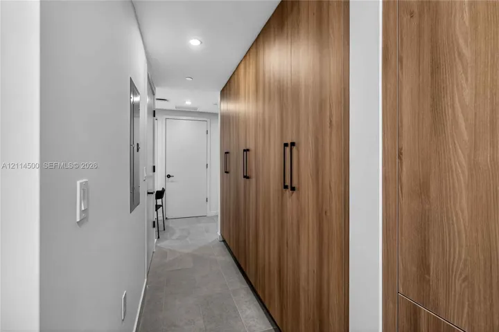 Full-height wall cabinetry with wood-finish paneling, matte black hardware, recessed ceiling lighting, and large-format tile flooring