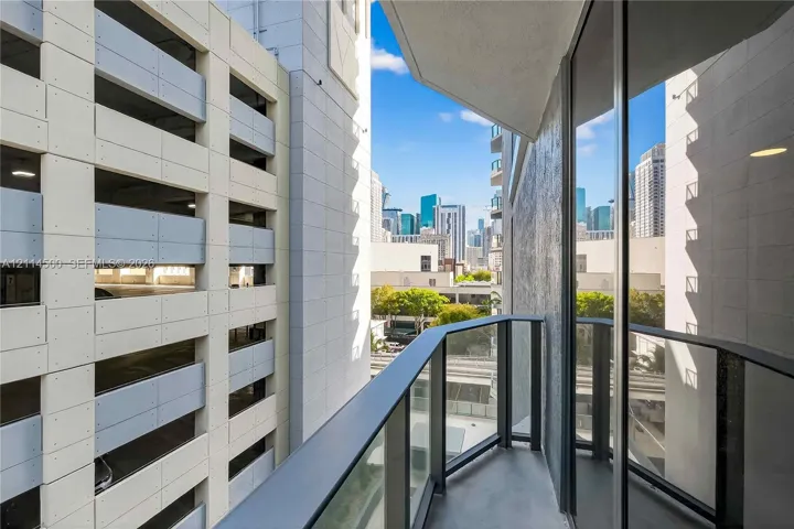 Covered balcony with black metal railings and glass panels, featuring urban skyline surroundings