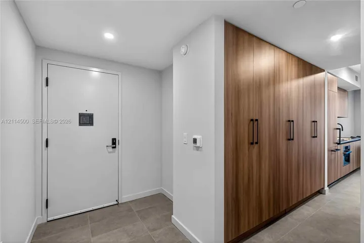 Entryway featuring large-format tile flooring, recessed ceiling lighting, and a floor-to-ceiling wood-finish cabinetry wall with matte black hardware