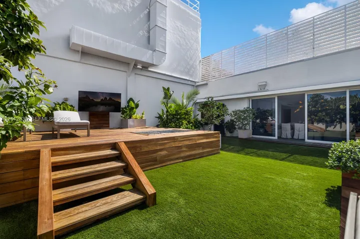 Outdoor courtyard featuring a multi-level wood deck, built-in recessed fire feature, synthetic lawn, and perimeter privacy fencing