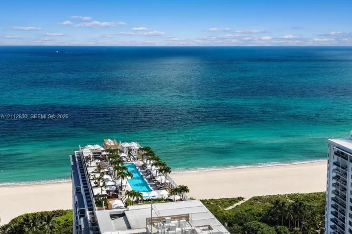 Elevated oceanfront terrace featuring an expansive lap pool, integrated palm tree landscaping, and paved sun deck surfaces