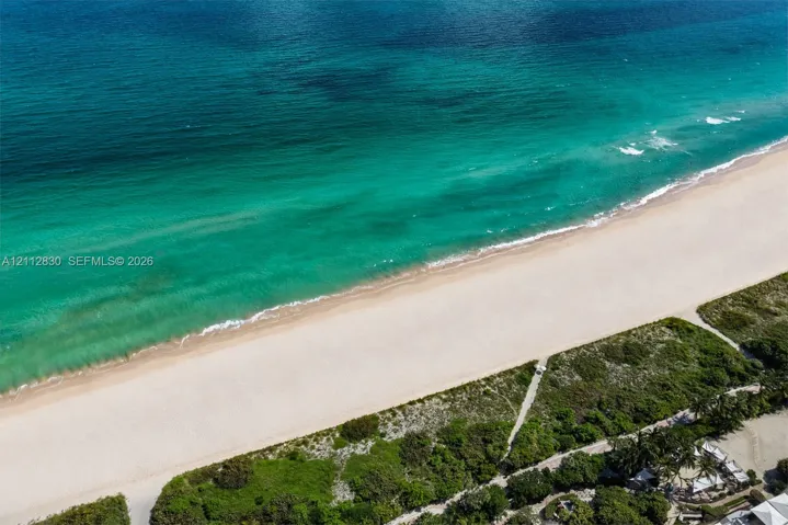 Direct oceanfront access featuring expansive sandy shoreline, turquoise water, and native coastal vegetation