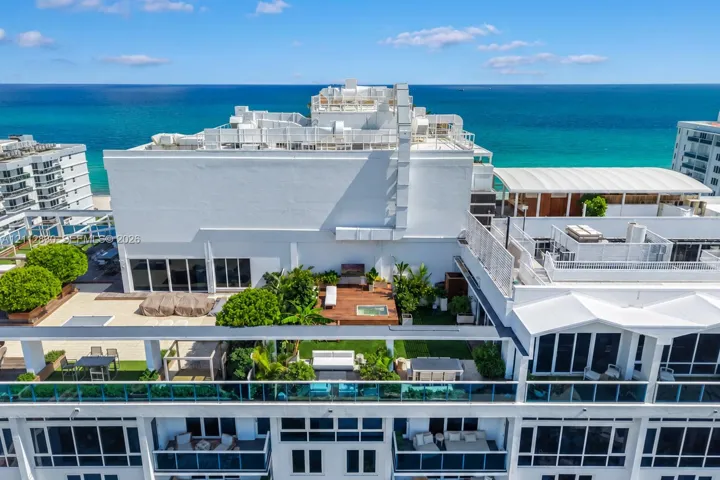 Rooftop terrace featuring wood decking, built-in hot tub, landscaping, glass railings, and ocean backdrop