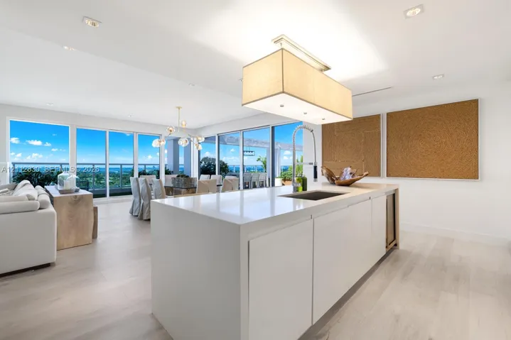 Kitchen island with stone-finish countertop, integrated sink, and built-in under-counter beverage chiller, complemented by wood-finish flooring, recessed lighting, and floor-to-ceiling glass paneling