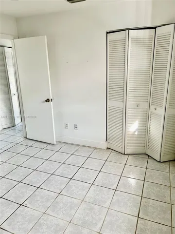 Neutral-toned tile flooring, white accordion-style louvered closet doors, and interior paneled doors