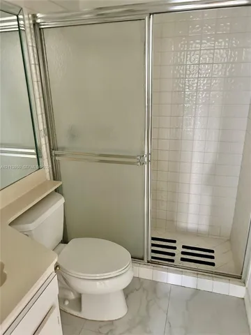 Bathroom featuring a shower stall with a sliding glass door and tiled surround, white vanity, and stone-finish flooring
