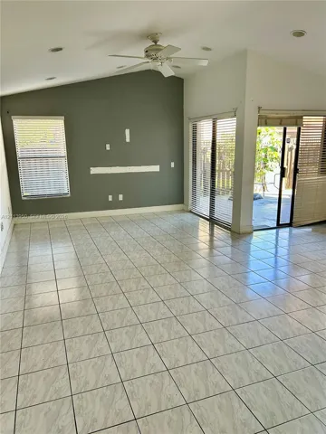 Vaulted ceiling with a central paddle fan, tile flooring, and glass sliding doors