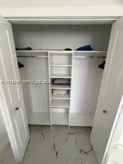 Walk-in closet featuring white-finish built-in shelving, two overhead storage ledges, metal hanging rods, and large-format tile flooring with a veined pattern