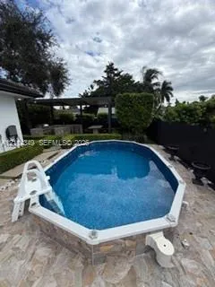 Oval swimming pool with tile-surfaced exterior, stone-paver decking, and a covered outdoor structure featuring built-in masonry elements