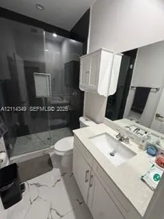 Bathroom featuring a glass-enclosed shower with tile surround, white cabinetry, integrated sink with stone-finish countertop, and large-format porcelain tile flooring