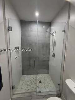 Walk-in shower featuring a glass enclosure, gray tile surround, pebble-style floor, built-in recessed niche, and handheld shower fixture