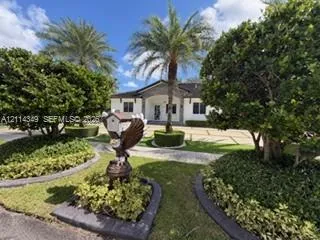 Exterior facade featuring a paved driveway, manicured landscaping, stone garden borders, and mature palm trees