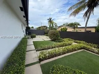 Landscaped backyard featuring tiered turf lawn sections, linear concrete pavers, structured hedge borders, and a privacy fence