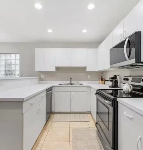 Kitchen featuring white cabinetry, solid-surface countertops, recessed ceiling lighting, a stainless steel over-the-range microwave, and ceramic tile flooring