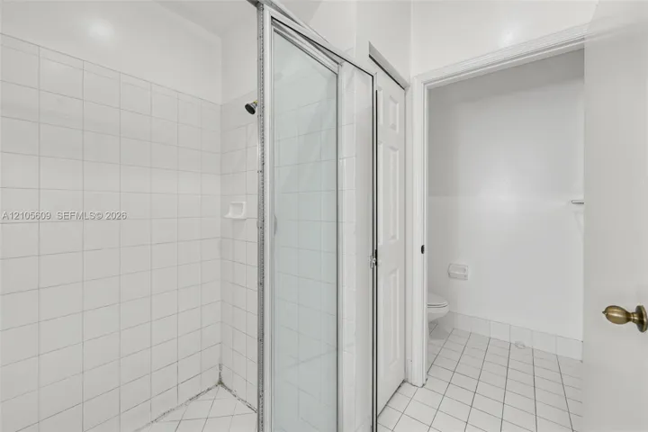 Shower stall with a glass door, white wall tiling, and white floor tiling