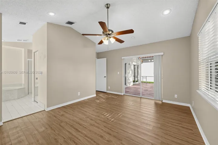 Vaulted ceiling with recessed lighting and a brushed-nickel ceiling fan, wood-finish flooring, and sliding glass doors