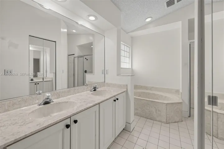 Dual-sink vanity with stone-finish countertop, full-width mirror, recessed lighting, and separate built-in soaking tub with surround