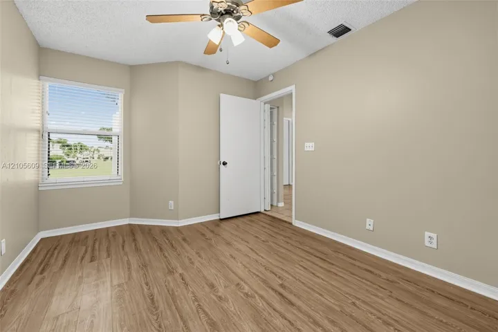 Neutral-toned interior space featuring wood-finish flooring, a multi-pane window, and a ceiling-mounted light fixture with a central fan